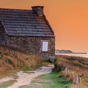 la maison du douanier à Quimiac sur fond de ciel orange crépusculaire et port de Piriac au loin