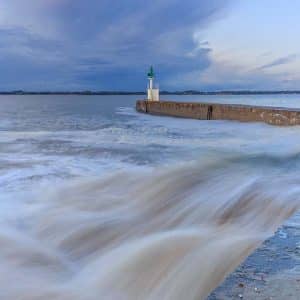 Phare de Merquel au coucher du soleil après la tempête avec effet cascade sur les vagues de la jetée en pose longue